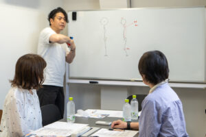 ホワイトボードで図解しながら日本人の骨格と反り腰のメカニズムを解説する講師
